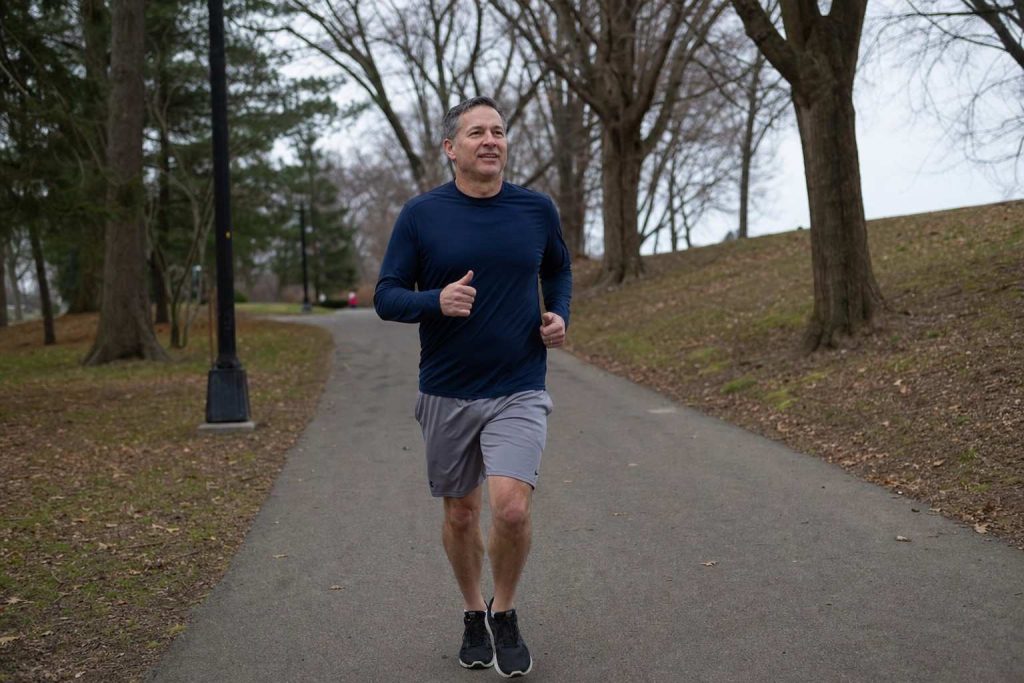 A relaxed recreational runner around 50 running comfortably on a neighborhood park path